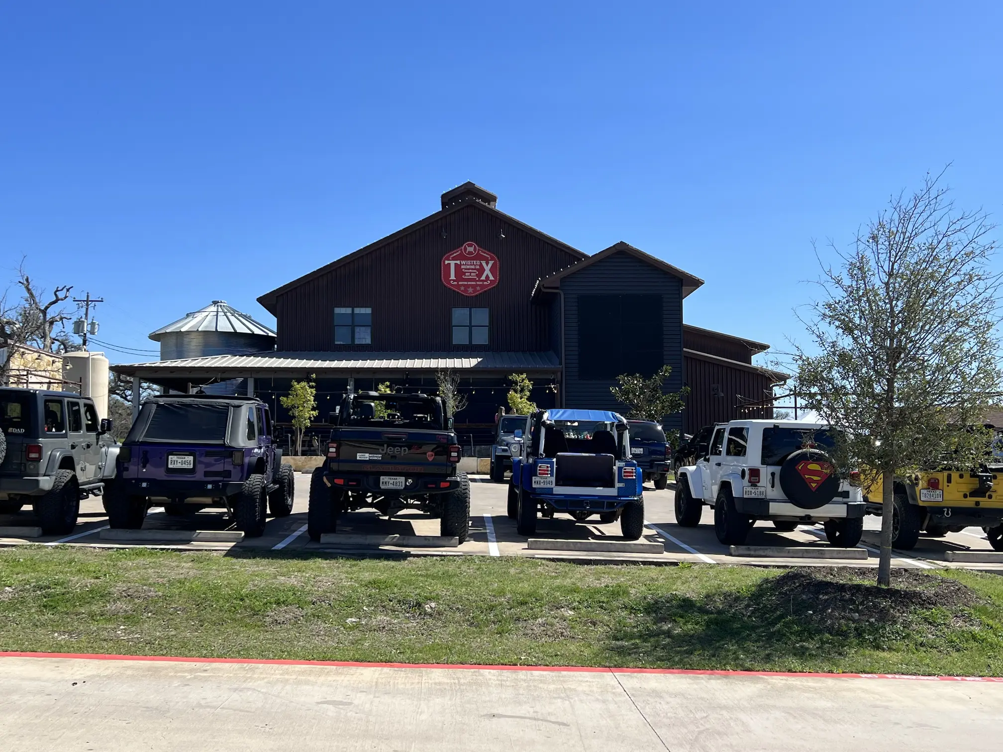 Exterior view of Twisted X Brewery with a row of parked Jeeps in front, under a clear blue sky.