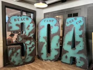 Large, weathered turquoise and brown metal letters spelling '30A' with 'Beach Camp Brew Co.' printed on them, displayed inside Beach Camp Brew Co. in Grayton Beach, Florida.